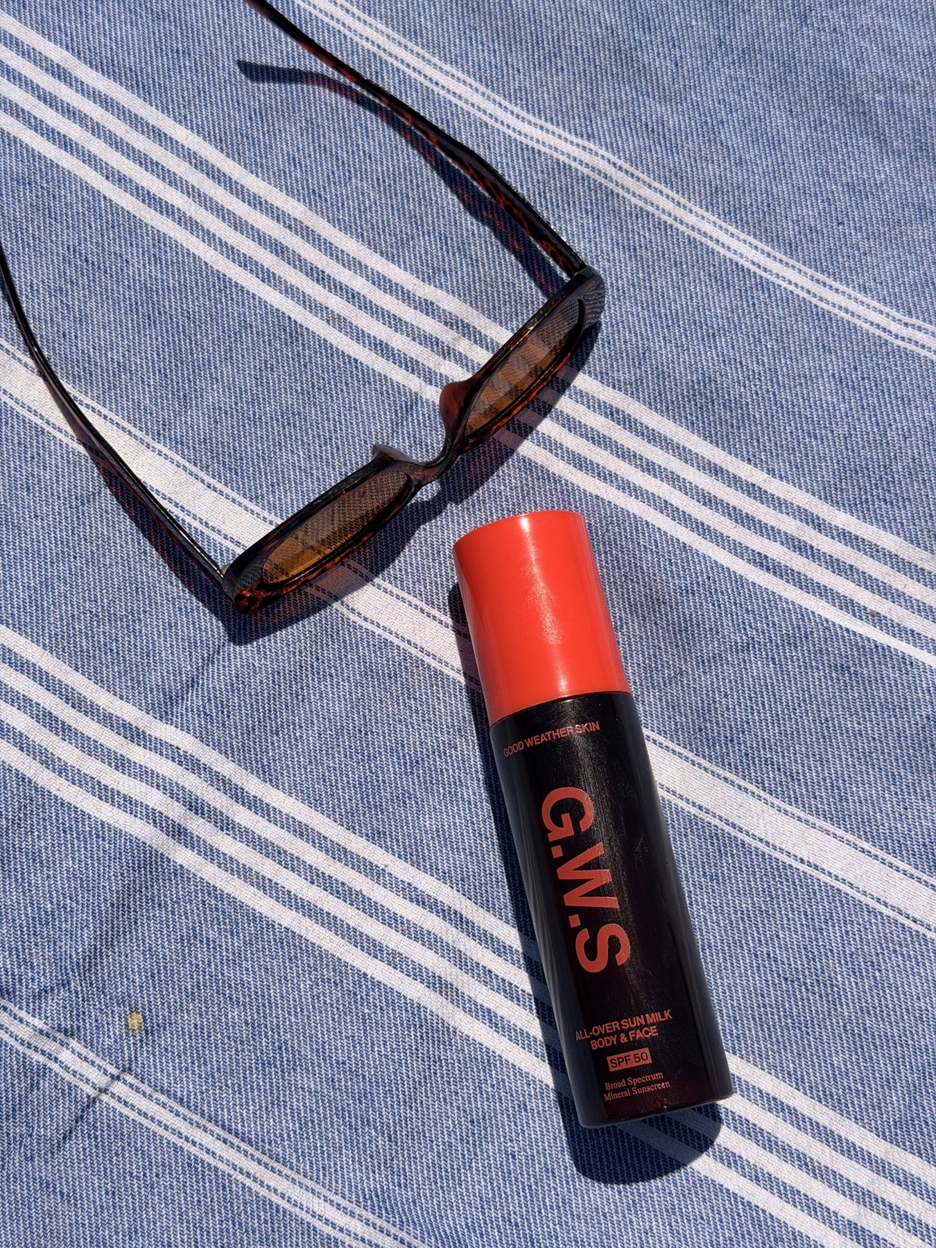Sunscreen and sunglasses on blue striped fabric